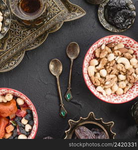 mixed nuts tea dried fruits metallic spoons black concrete backdrop