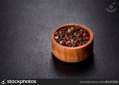 Mixed of diffrent kind peppercorns in wooden bowl on black background. Black, red and white pepper in bowl on f black concrete background