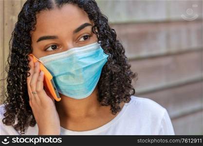 Mixed race African American teenager teen girl young woman wearing a face mask and talking on mobile cell phone during the Coronavirus COVID-19 pandemic