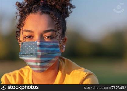 Mixed race African American teenager teen girl young woman wearing a face mask decorated with the American US flag outside during the Coronavirus COVID-19 pandemic