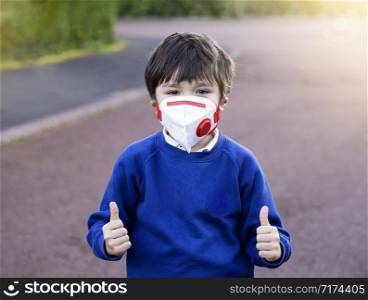 Mixed race asian - caucasian 6 year old, Child showing thumb up wearing protection face mask pollution or virus while walking to school, Concept for Protecting Corona or Coronava virus and pm 2.5