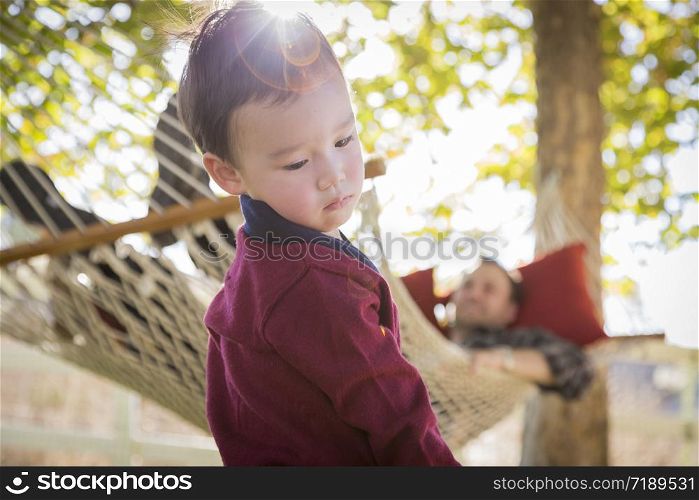 Mixed Race Boy Having Fun Outside While Parent Watches From Behind in a Hammock.