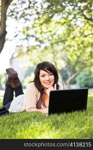 Mixed race college student lying down on the grass working on laptop at campus