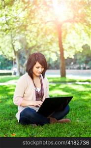 Mixed race college student sitting on the grass working on laptop at campus
