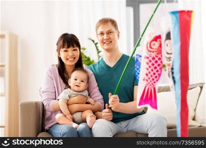 mixed-race family, children&rsquo;s day and asian holidays concept - happy mother, father and baby son with koinobori carp streamer celebrating tango no sekku at home. mixed-race family with koinobori carp streamer
