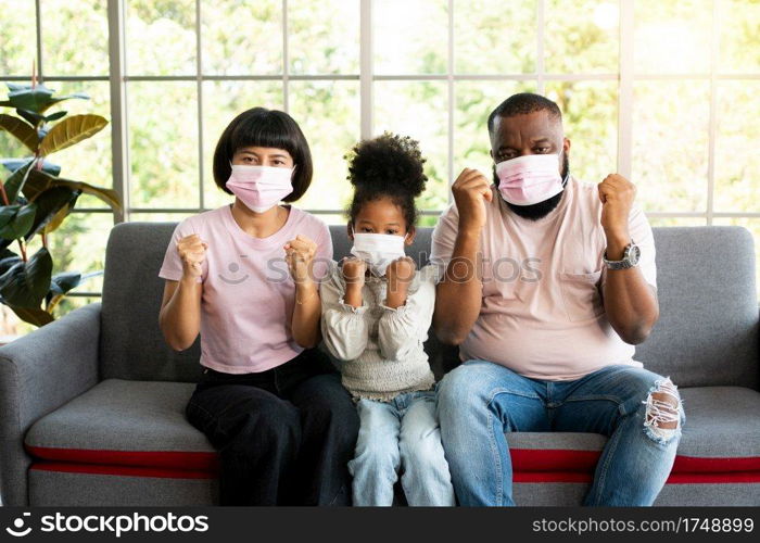 Mixed Race family sitting on the sofa and wearing medical face masks for against coronavirus world pandemic and stay quarantined together at home social distancing new normal lifestyle