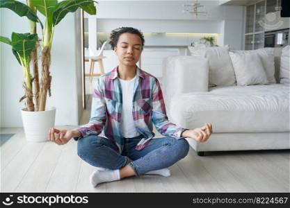 Mixed race girl practices yoga, meditates, breathing clean air on floor at home. African american young woman, sitting in lotus pose with mudra gesture while meditation. Healthy lifestyle, wellness.. Mixed race girl practices yoga, meditates, breathing clean air on floor at home. Healthy lifestyle