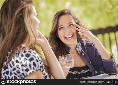 Mixed Race Girls Talking on Thier Mobile Cell Phones Sitting Outside at a Table.