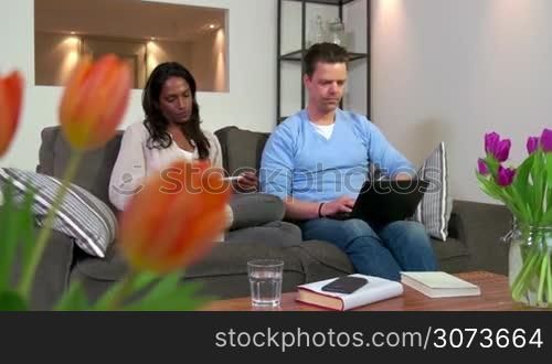 Mixed race heterosexual couple, people on sofa, marriage relationship with young husband and wife. Angry man and woman arguing, fighting at home. Domestic problems, loud talking and screaming