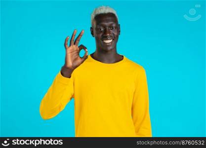 Mixed race man showing thumb up sign over blue background. Positive african guy smiles to camera. Winner. Success. Body language. Mixed race man showing thumb up sign over blue background. Positive african guy smiles to camera. Winner. Success. Body language.