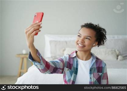 Mixed race teen girl blogger chatting online by phone video call, using modern mobile apps at home. Friendly smiling biracial teenager lady holding smartphone, takes a selfie photography.. Mixed race teen girl blogger chatting online by phone video call, using modern mobile apps at home