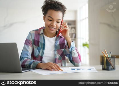 Mixed race teen girl school student call by phone, discussing homework with friend, sitting at desk with laptop. Smiling biracial schoolgirl chatting with classmate by mobile while learning at home.. Mixed race teen girl school student call by phone, discussing homework with friend, sitting at desk