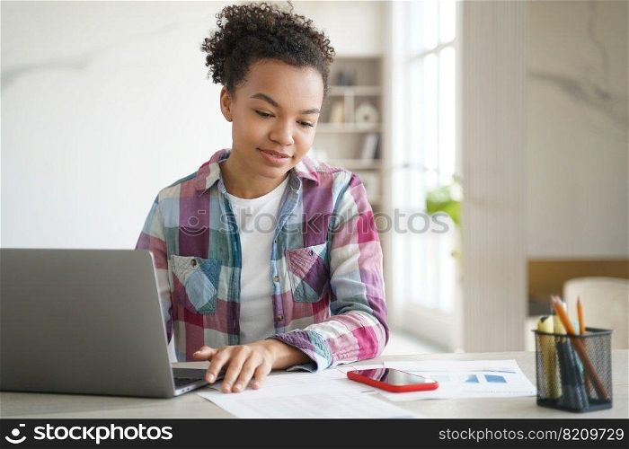 Mixed race teen girl student learning at laptop look on mobile phone, reading message in social networks. Modern biracial schoolgirl distracted from study, homework. Gadget addiction concept.. Mixed race teen girl student learning at laptop look on mobile phone, read message in social network