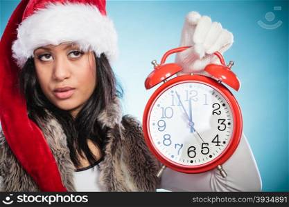 Mixed race woman in santa hat with alarm clock.. Cute woman in santa claus hat holding alarm clock. Mixed race african girl on blue. Christmas time season concept.