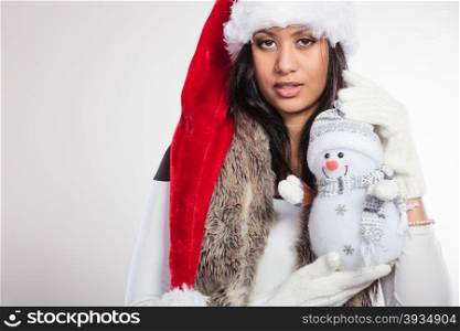 Mixed race woman in santa hat with little snowman.. Cute lovely woman in santa claus hat holding little snowman. Attractive mixed race african girl in studio on gray. Christmas season.