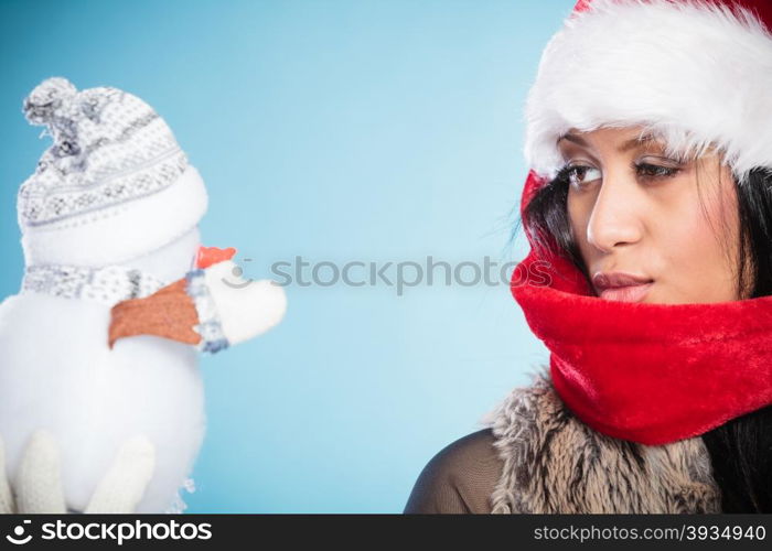 Mixed race woman in santa hat with little snowman.. Cute lovely woman in santa claus hat holding little snowman. Attractive mixed race african girl in studio on blue. Christmas season.