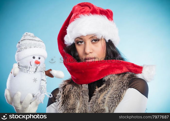 Mixed race woman in santa hat with little snowman.. Cute lovely woman in santa claus hat holding little snowman. Attractive mixed race african girl in studio on blue. Christmas season.