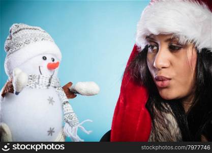 Mixed race woman in santa hat with little snowman.. Cute lovely woman in santa claus hat holding little snowman. Attractive mixed race african girl in studio on blue. Christmas season.