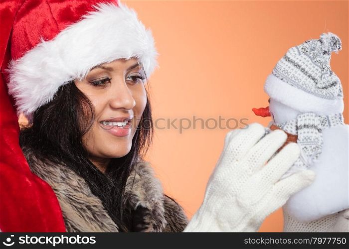 Mixed race woman in santa hat with little snowman.. Smiling cute woman in santa claus hat holding little snowman. Attractive mixed race african girl in studio on orange. Christmas season.