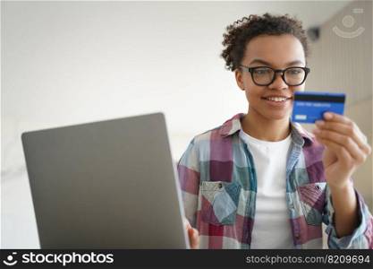 Mixed race young girl holding credit card, using online banking services at laptop, making payment. Smiling teen lady wearing glasses paying using e-bank at home. E-banking, e-commerce concept.. Mixed race teen girl holds credit card, using online banking services at laptop at home. E commerce