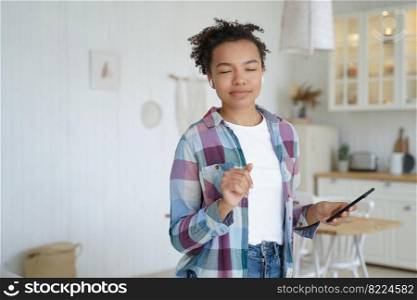 Mixed race young girl in wireless earphones dancing at home, holding smartphone, listening to music relaxing at home. Happy teen lady in earbud enjoying sound, playlist, using mobile musical apps.. Dancing mixed race girl listens to music, holding phone, enjoying sound, using musical apps at home
