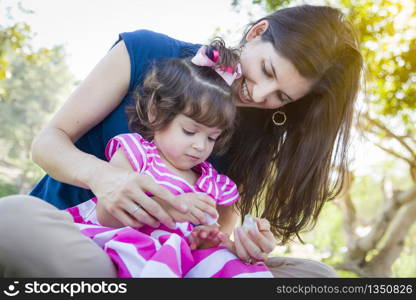 Mixed Race Young Mother and Cute Baby Girl Applying Fingernail Polish in the Park.