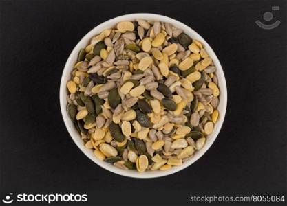 mixed seeds and nuts in ceramic white bowl on dark background