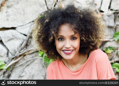 Mixed woman with afro hairstyle standing in an urban park. Young girl smiling.