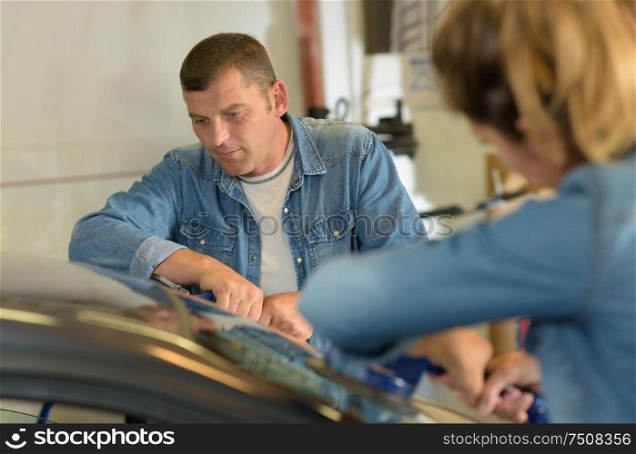 mle and female mechanics fitting a new car windscreen