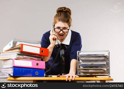 Mobbing at work, bad job relations concept. Angry mad bossy businesswoman talking on phone sitting working at desk full off documents in binders.. Angry bossy businesswoman phone talking