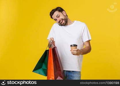 Mobile app for online shopping. Joyful happy man in casual white t-shirt holding cell phone and packages, smiling at camera. Mobile app for online shopping. Joyful happy man in casual white t-shirt holding cell phone and packages, smiling at camera.