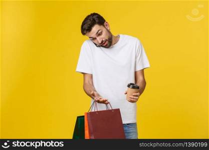 Mobile app for online shopping. Joyful happy man in casual white t-shirt holding cell phone and packages, smiling at camera. Mobile app for online shopping. Joyful happy man in casual white t-shirt holding cell phone and packages, smiling at camera.