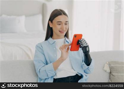 Mobile apps for disabled people. Happy girl with artificial hand using smartphone, chatting or shopping online at home. Modern woman with disability holding phone by bionic prosthetic arm.. Girl holding smartphone using bionic prosthetic arm at home. Mobile apps for disabled people