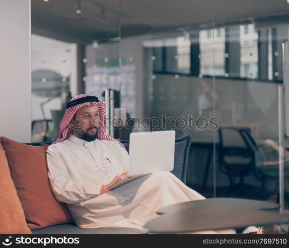 Mobile business communication and entrepreneurship. Arab businessman talking on smartphone and using a laptop computer, alone at open space coworking workplace or home office in the night. . Mobile business communication and entrepreneurship. Arab businessman talking on smartphone and using laptop computer at workplace at home office