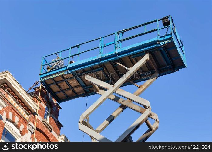 Mobile elevating work platform with builders repairing the roof of old historic house in Tilburg, the Netherlands. Work platform with builders repairing roof historic Dutch house