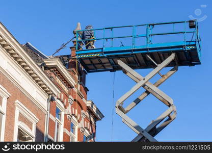 Mobile elevating work platform with builders repairing the roof of old historic house in Tilburg, the Netherlands. Work platform with builders repairing roof historic Dutch house