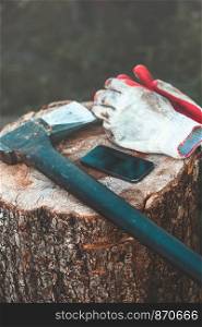 Mobile phone and tools, axe, work gloves on tree trunk