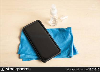 Mobile phone, cloth and alcohol spray bottle on table. Clean smartphone concept