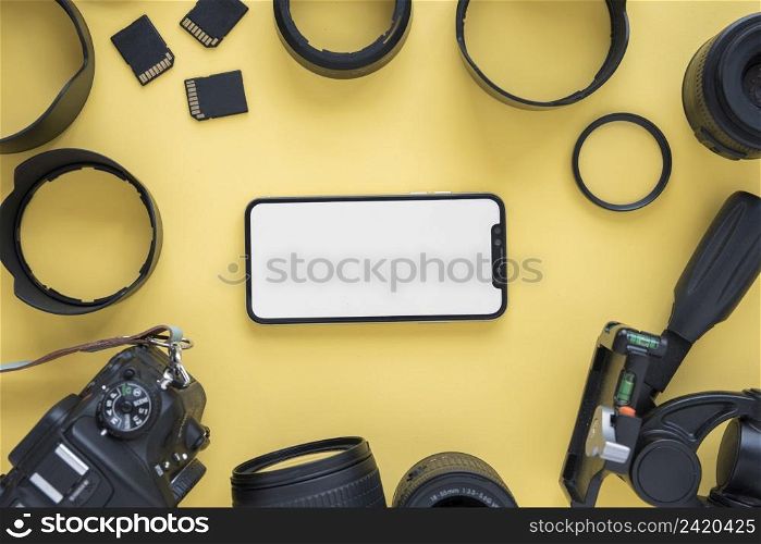 mobile phone with blank screen surrounded by modern camera accessories yellow background