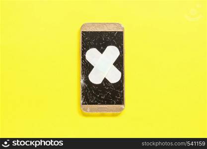 Mobile Smart Phone with cracked screen fixed with plaster on yellow background Concept Flat Lay. Mobile Smart Phone with cracked screen fixed with plaster on yellow