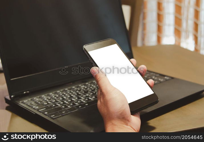 mock up hand holding smartphone white blank screen and computer laptop on the desk.