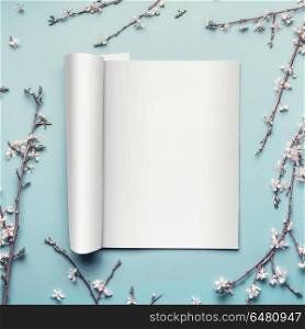 Mock-up of open magazine or catalog on pastel blue desktop background with twigs and white cherry blossom, top view, flat lay