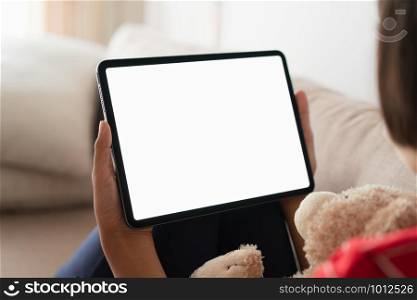 Mockup, Blank digital tablet in the hand of Asian little girl, Tablet white screen. While sitting on the sofa at her home.