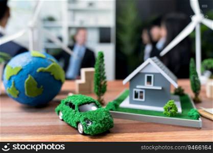Mockup electric car with eco-friendly energy infrastructure on table with blurred background of productive business team meeting to contribute natural preservation and sustainable future. Quaint. EV car model with mockup wind turbine on blurred background meeting. Quaint