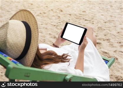 Mockup image of a woman holding a black tablet pc with blank desktop screen while lying down on a beach chair