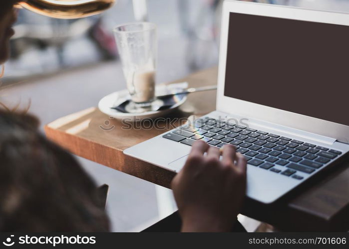 Mockup image of a woman using laptop with blank screen and drinking latte caffe in the restaurant.