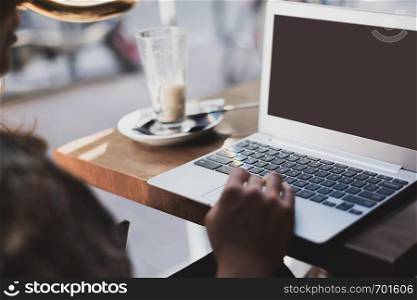 Mockup image of a woman using laptop with blank screen and drinking latte caffe in the restaurant.