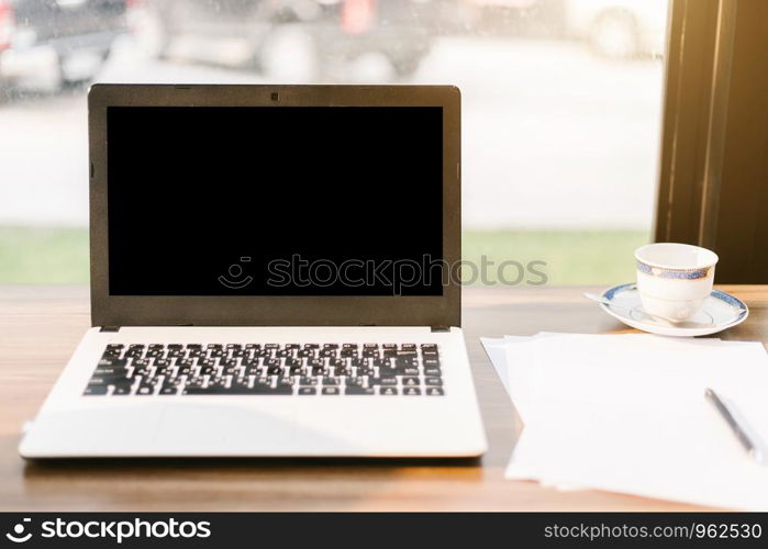 Mockup image of laptop with blank black screen,smart phone and document on wooden table of In the coffee shop.