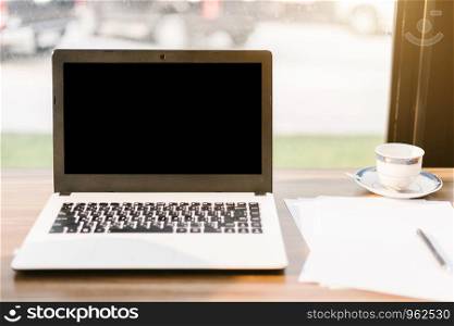 Mockup image of laptop with blank black screen,smart phone and document on wooden table of In the coffee shop.