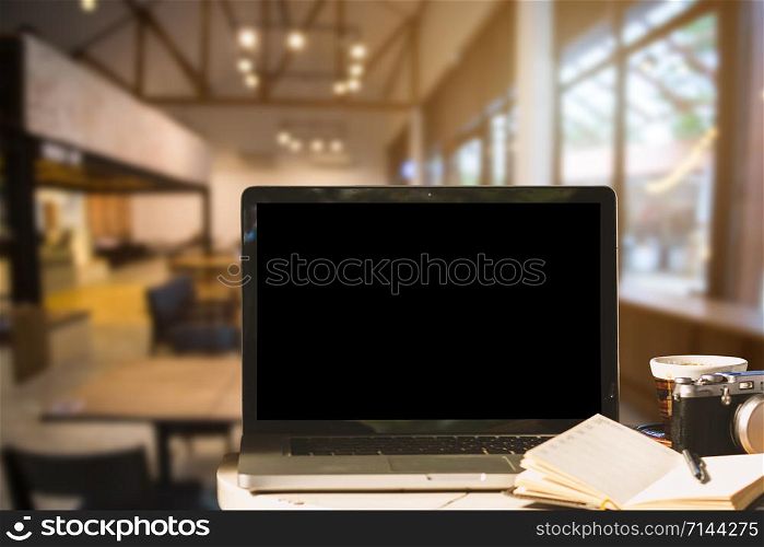 Mockup image of laptop with blank black screen with camera,notebook,coffee cup on wooden table of In the coffee shop background.